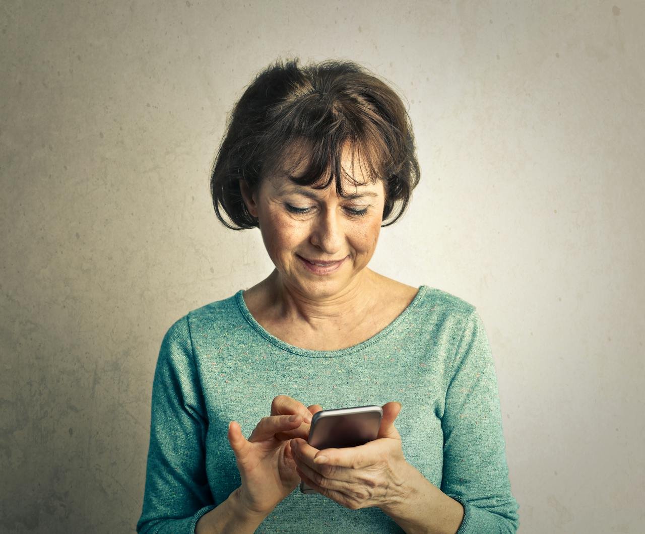 A senior woman smiling as she interacts with her smartphone indoors, expressing happiness and technology use.